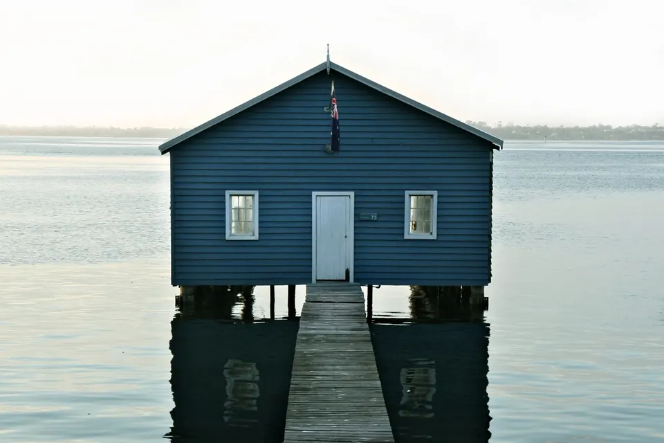 A small blue house on a pier over calm water