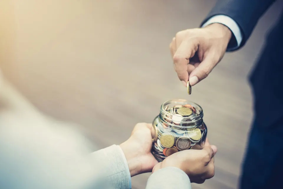 Hands placing a coin into a glass jar