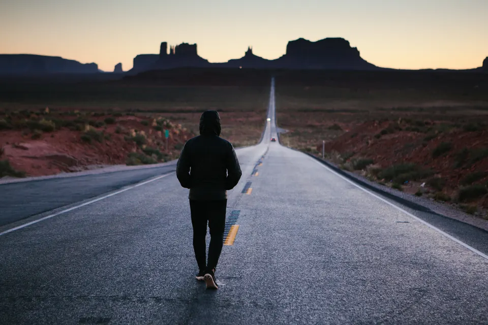 A person walking down an open road at dusk
