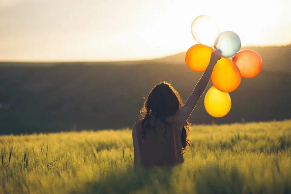 A woman holding balloons in a field at sunrise